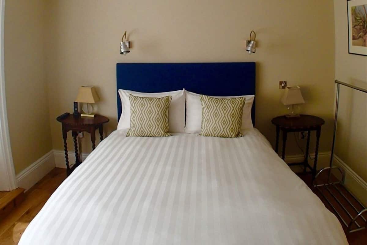 A neatly made bed with a blue headboard, two bedside lamps, and patterned pillows.