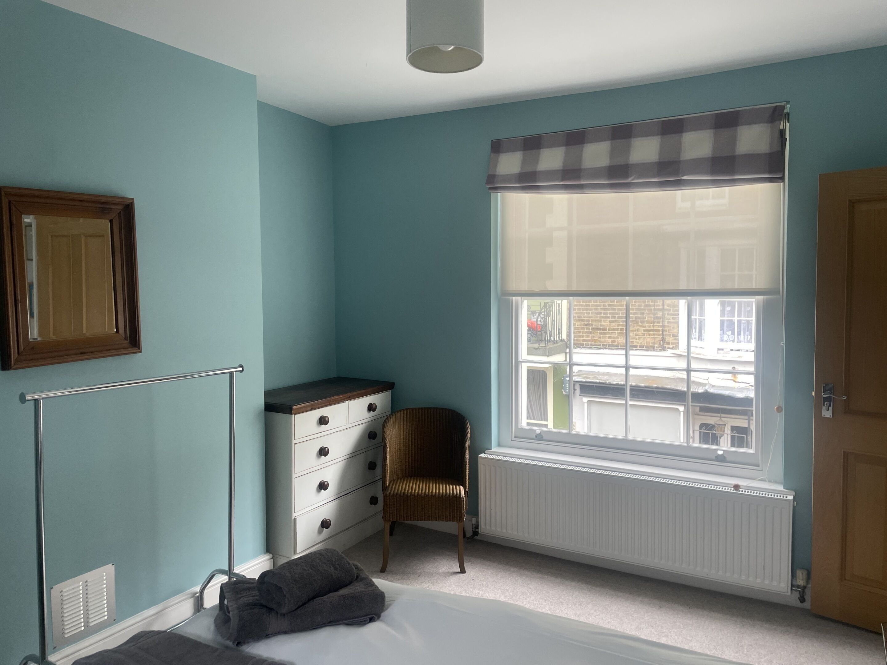 Une chambre à coucher comprenant un lit, une commode, une chaise, une fenêtre donnant sur un paysage agréable et un radiateur.