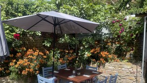 Un patio con una mesa y sillas, rodeado de plantas florecientes y un muro de ladrillo.