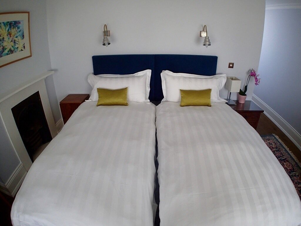 A double bed with white bedding and two gold pillows, a blue headboard, and two wall-mounted lamps.