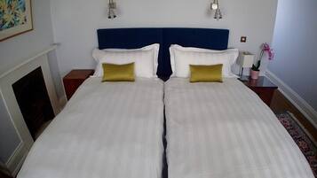 A double bed with white bedding and two gold pillows, a blue headboard, and two wall-mounted lamps.