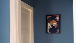 Un pasillo con una pared azul, una puerta blanca y un cuadro enmarcado en la pared.