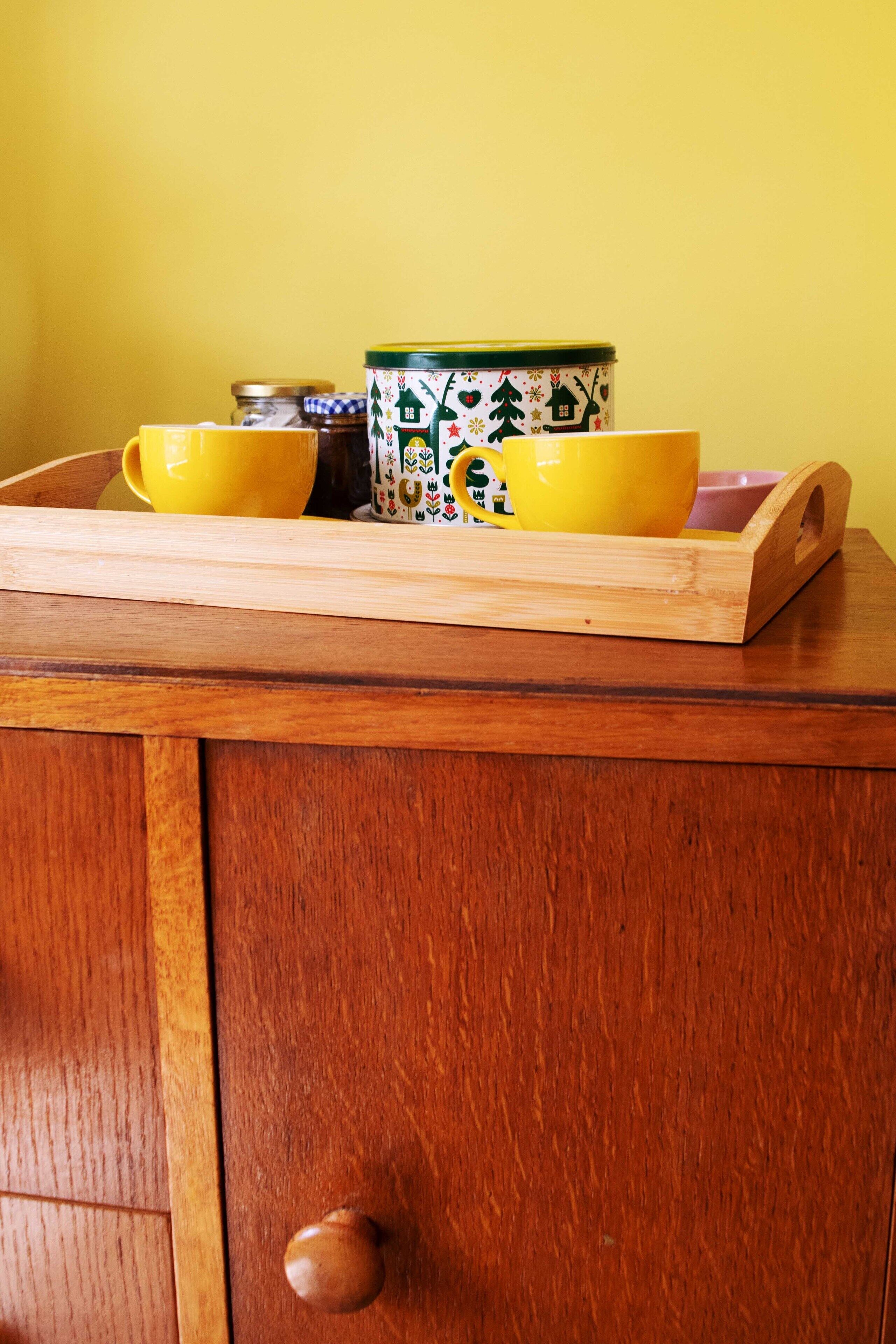 A wooden cabinet with a drawer containing a yellow tray holding a jar and a mug.
