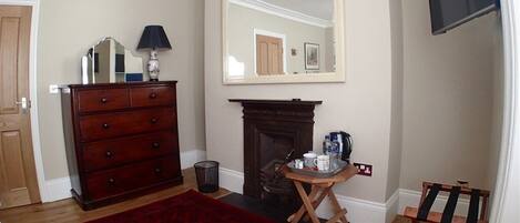 A room with a fireplace, a wooden dresser, a red patterned rug, a mirror, and a television mounted on the wall.