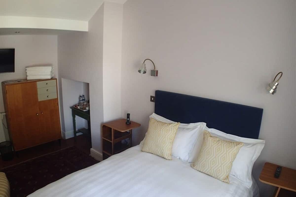 A hotel room with a bed, a wooden wardrobe, a small table, and a nightstand.