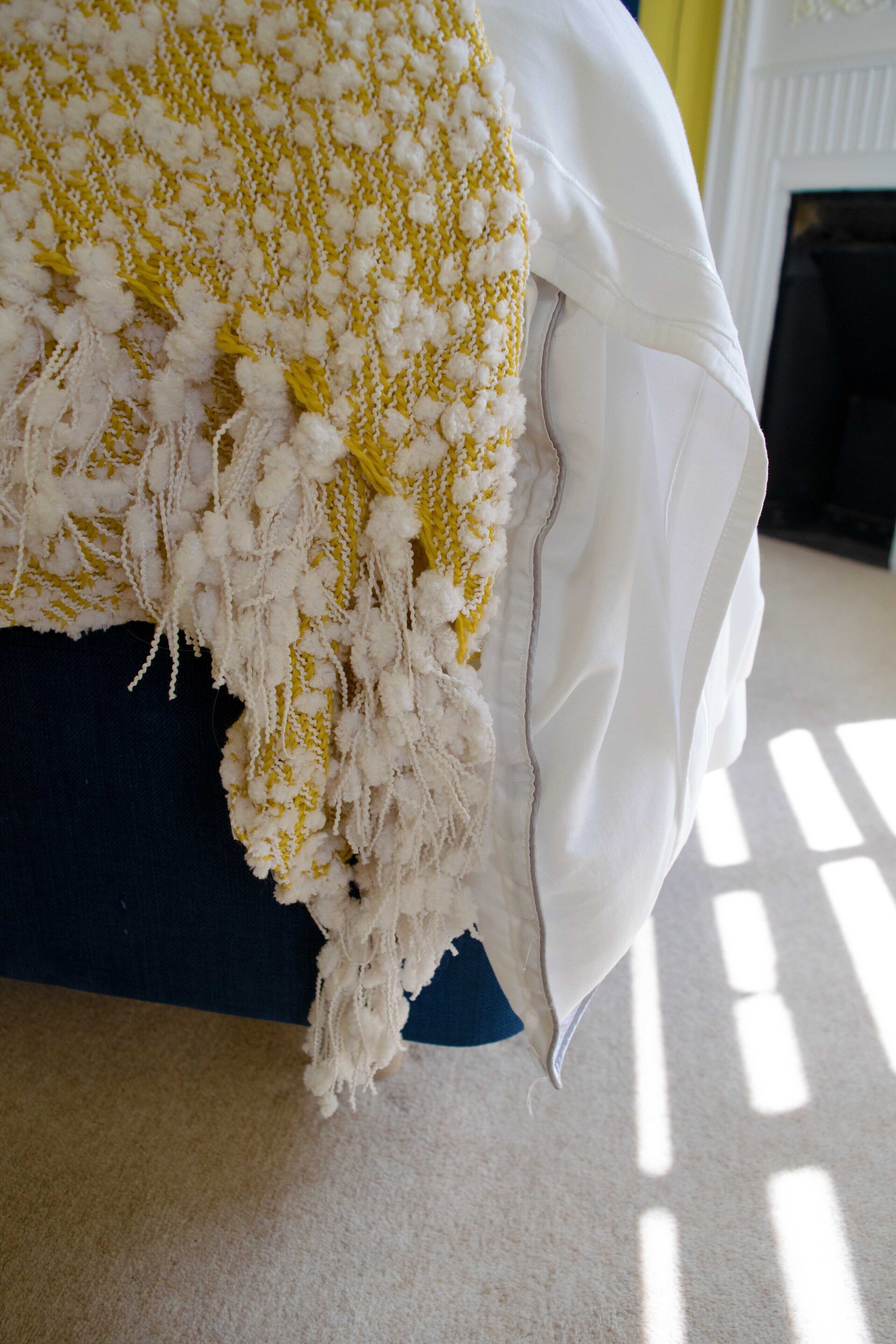A bed with a yellow and white patterned blanket and a white pillow.