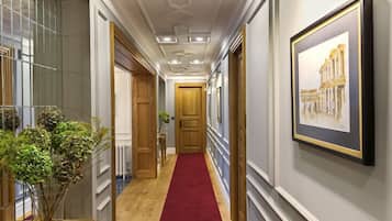 A hallway with a red carpet, wooden flooring, and a framed picture on the wall.