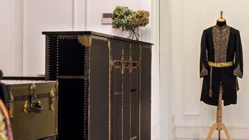 Un espace d’accueil avec un coffre noir et doré, un mannequin portant un manteau noir et un banc à motifs.