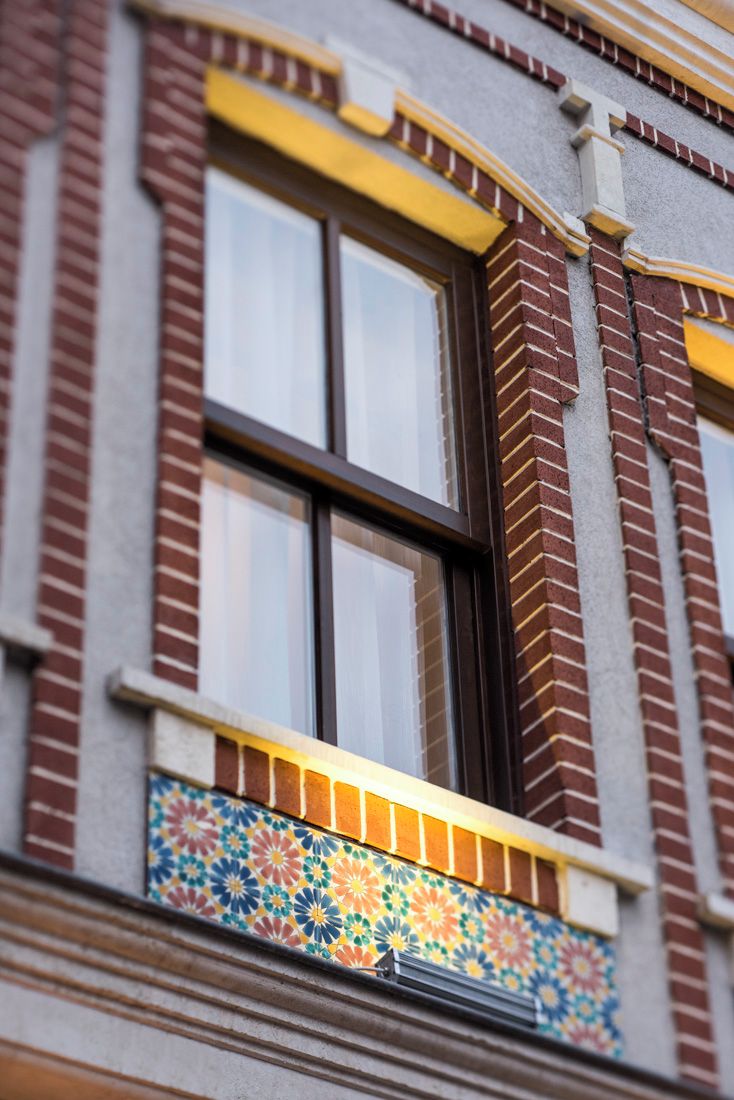 Fachada de edificio con una ventana que presenta un detalle decorativo amarillo y un colorido diseño de azulejos en la parte inferior.