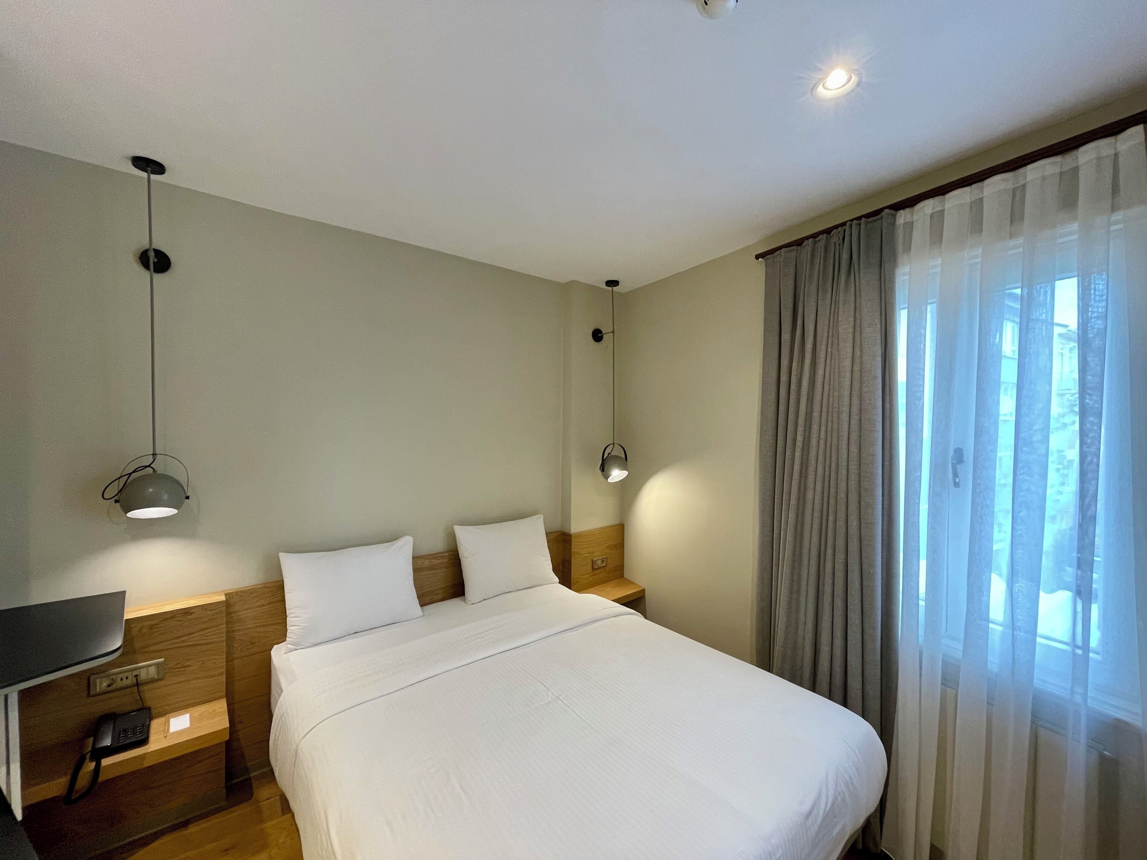 A hotel room with a bed, bedside tables, a desk, and a window with curtains.