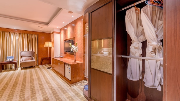 Habitación de hotel con un armario de madera, una tocador con espejo, un sofá, un escritorio y una bata colgada del armario.