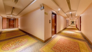 Un pasillo de hotel con alfombras estampadas, puertas de madera e iluminación empotrada en el techo.