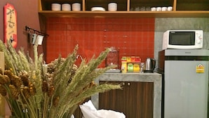 Een keuken met een magnetron, een koelkast en een plank met servies.
