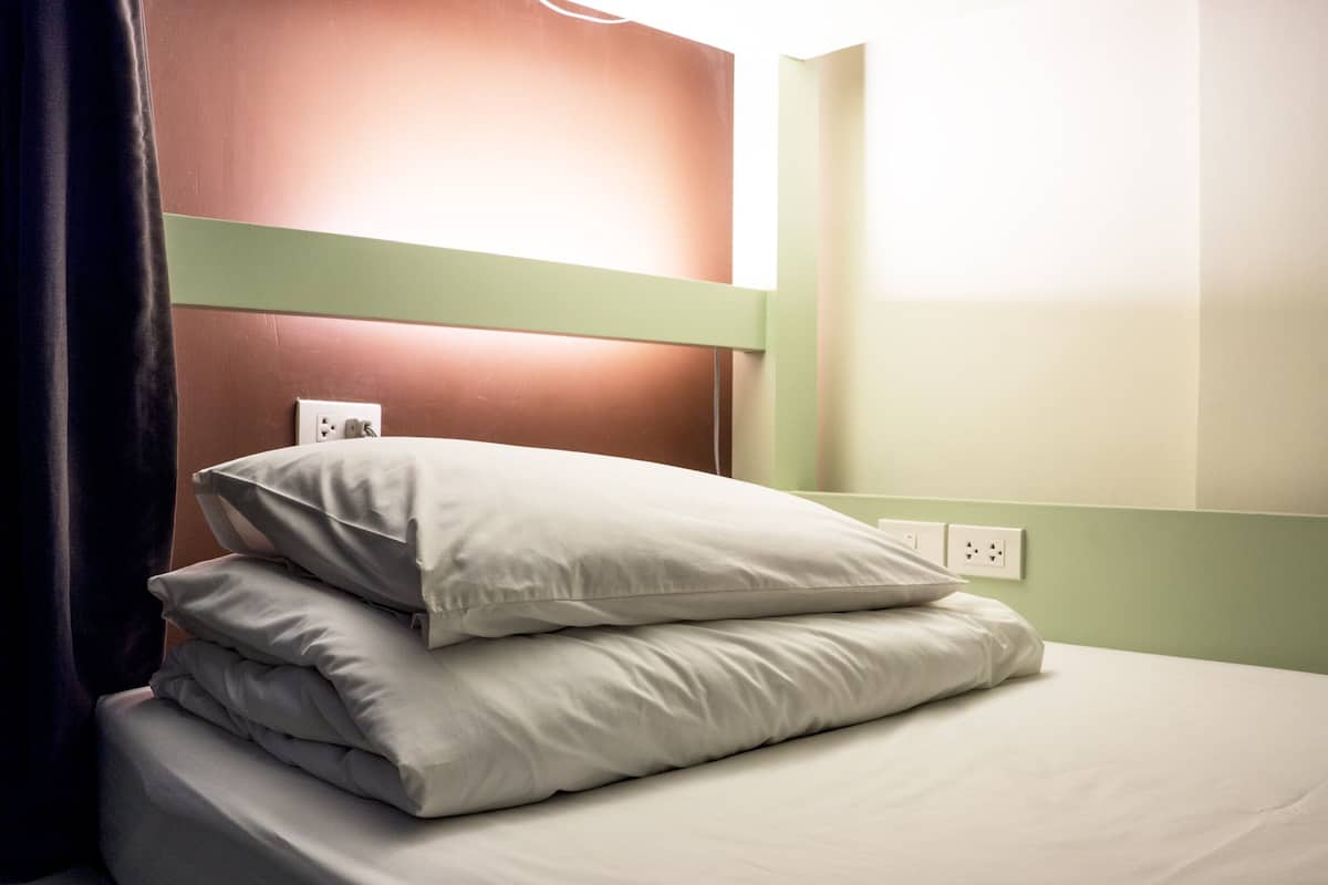 Een opgemaakt bed met kussens in een kamer met groene wanden en een bruin hoofdeinde.