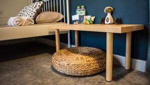 Een bed met hoofdeinde, een nachtkastje met een geweven mand en een klein plankje met spullen.