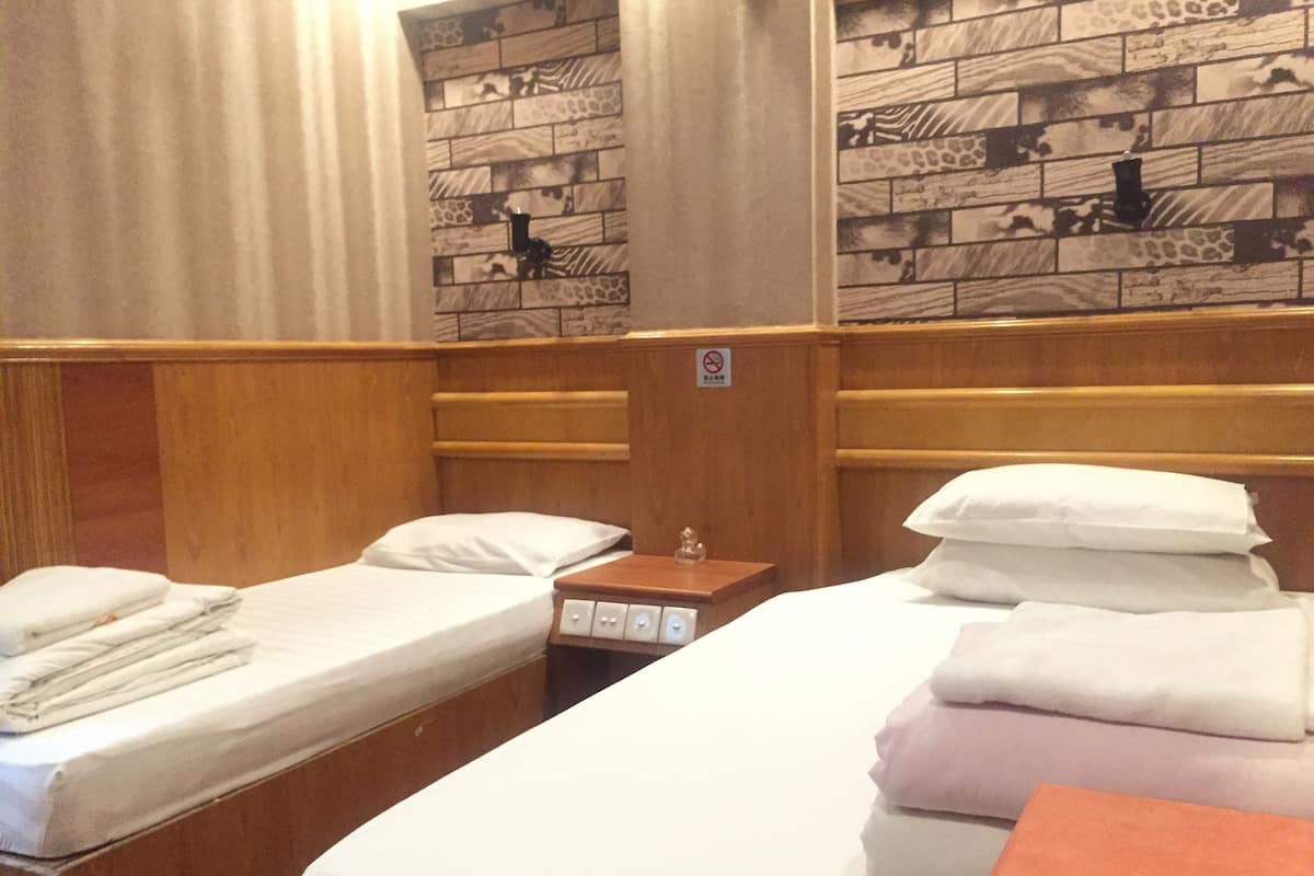 A hotel room with two single beds, wooden headboards, and a nightstand with a lamp.