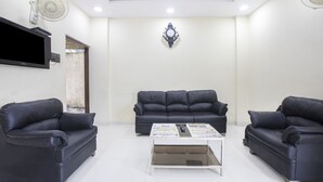 A modern living room with two black leather sofas, a coffee table, a flat-screen TV, and wall-mounted fans. - FabHotel Parimeet Navi Mumbai (Navi Mumbai)