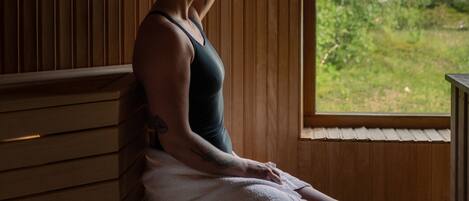 A person sitting by a window in a room with wooden walls and a bench.