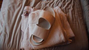 Una cama con una colcha a rayas, una toalla doblada y un par de pantuflas.