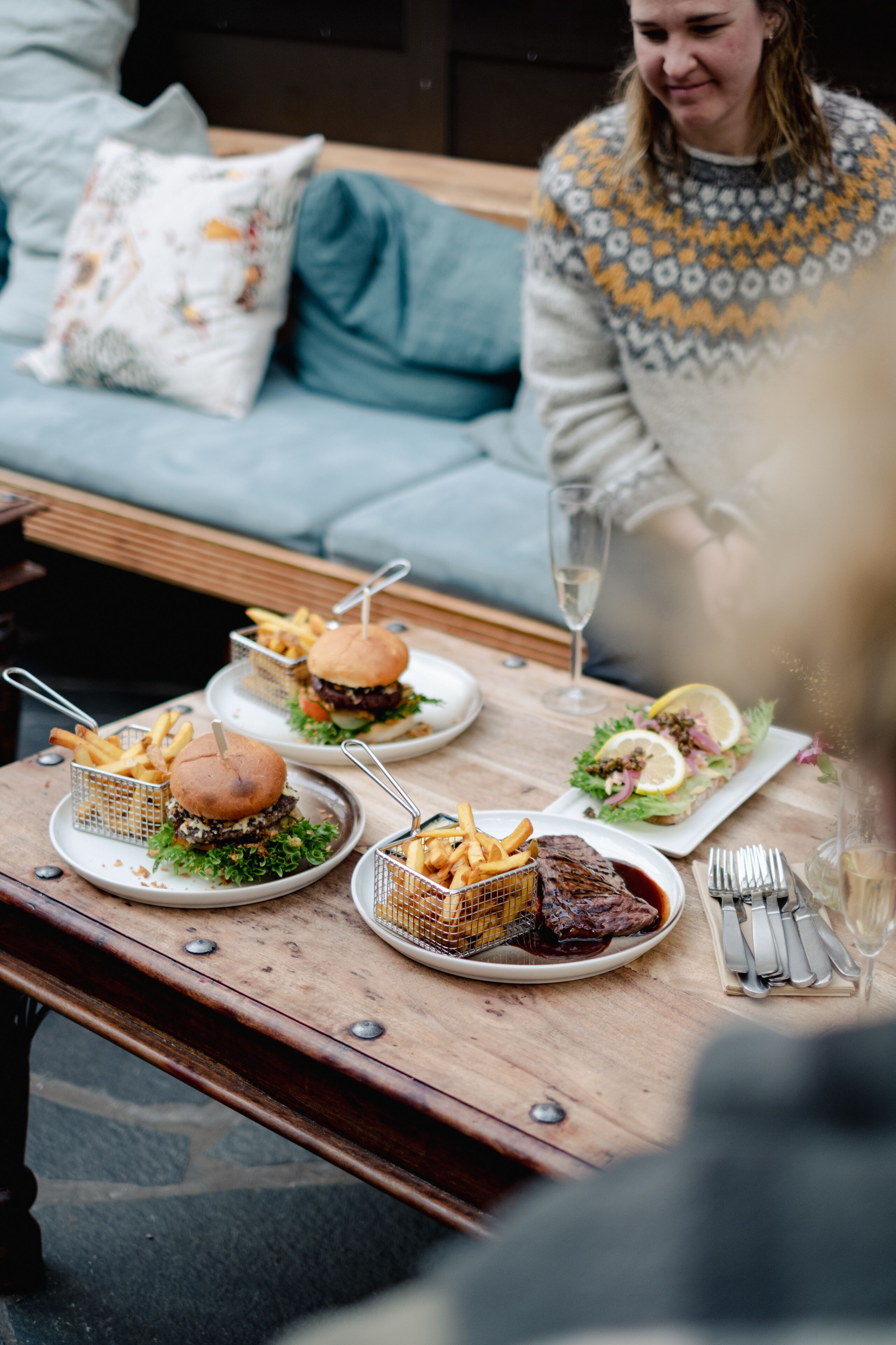 Una mesa de comedor con comida y bebidas, un sofá al fondo, y una persona visible solo parcialmente.