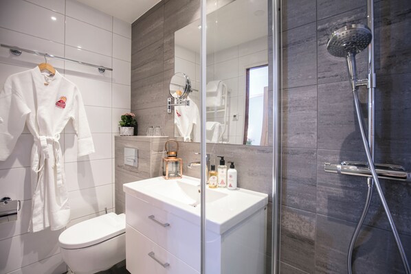 Un baño moderno con cabina de ducha de vidrio, un lavabo blanco y un inodoro.