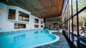 Una piscina interior con techo de madera y grandes ventanales.