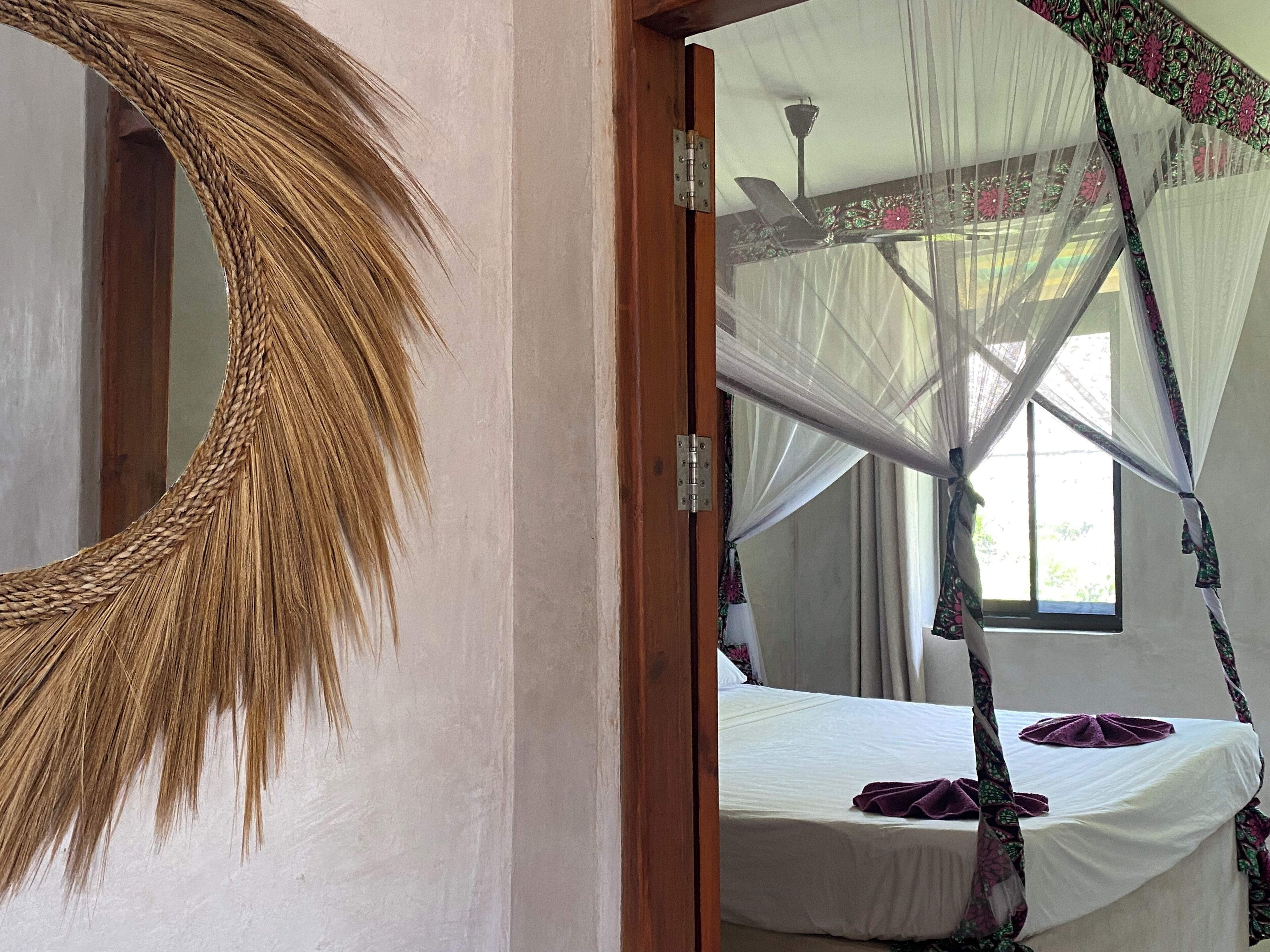 Une chambre avec un lit recouvert d’une moustiquaire, un grand miroir et une fenêtre avec des rideaux.
