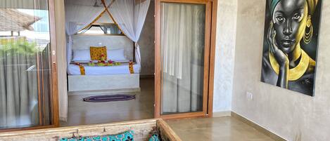 A room with a bed, a sofa, a painting, and a view through a glass door.