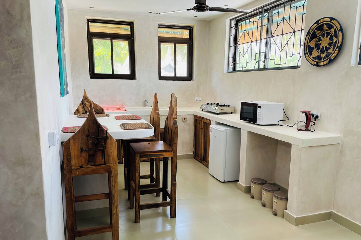 A compact kitchen with a dining table, chairs, a refrigerator, a microwave, and a gas stove.