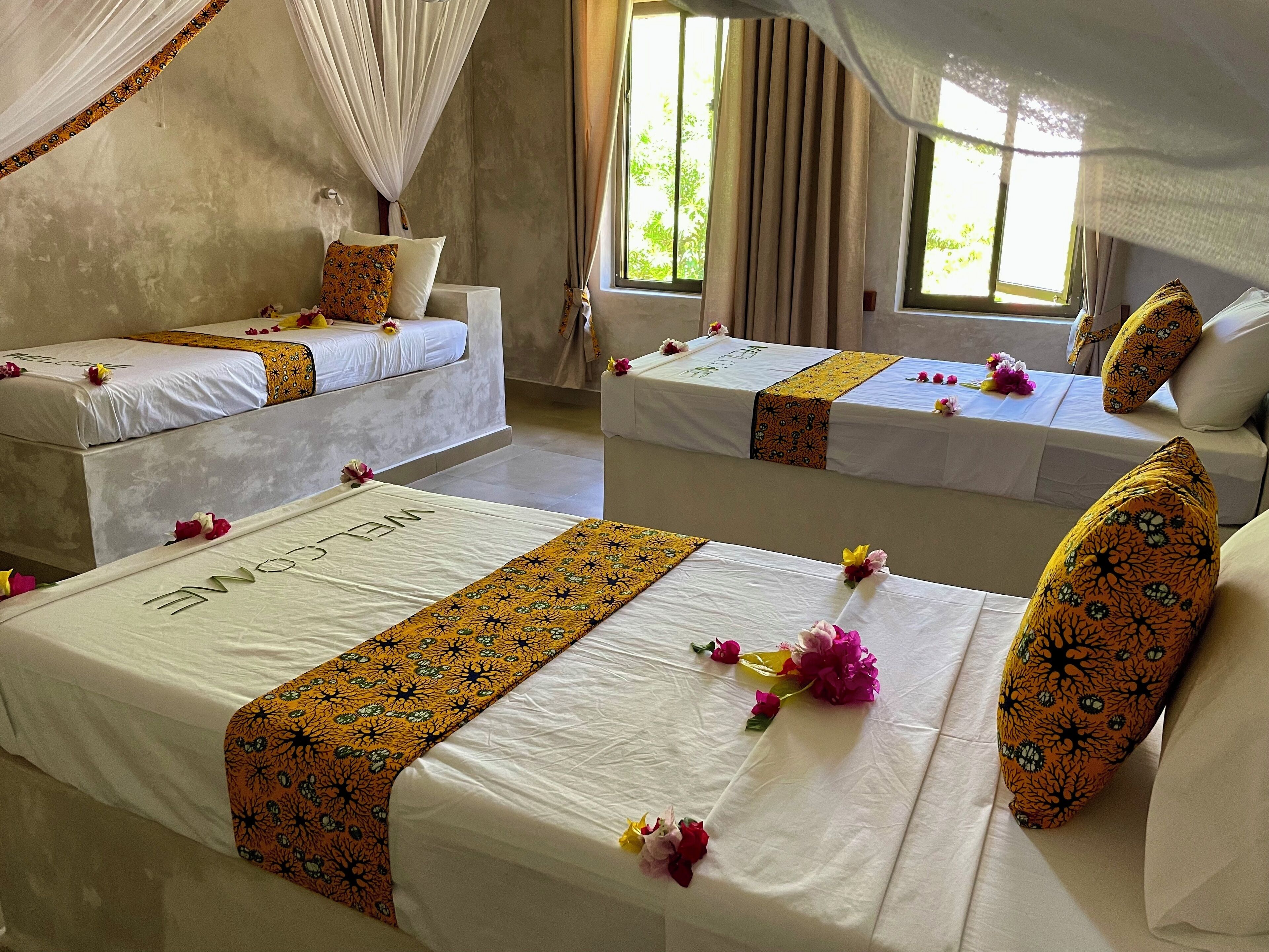 A hotel room with two beds, each with a white bedspread and a decorative orange runner.