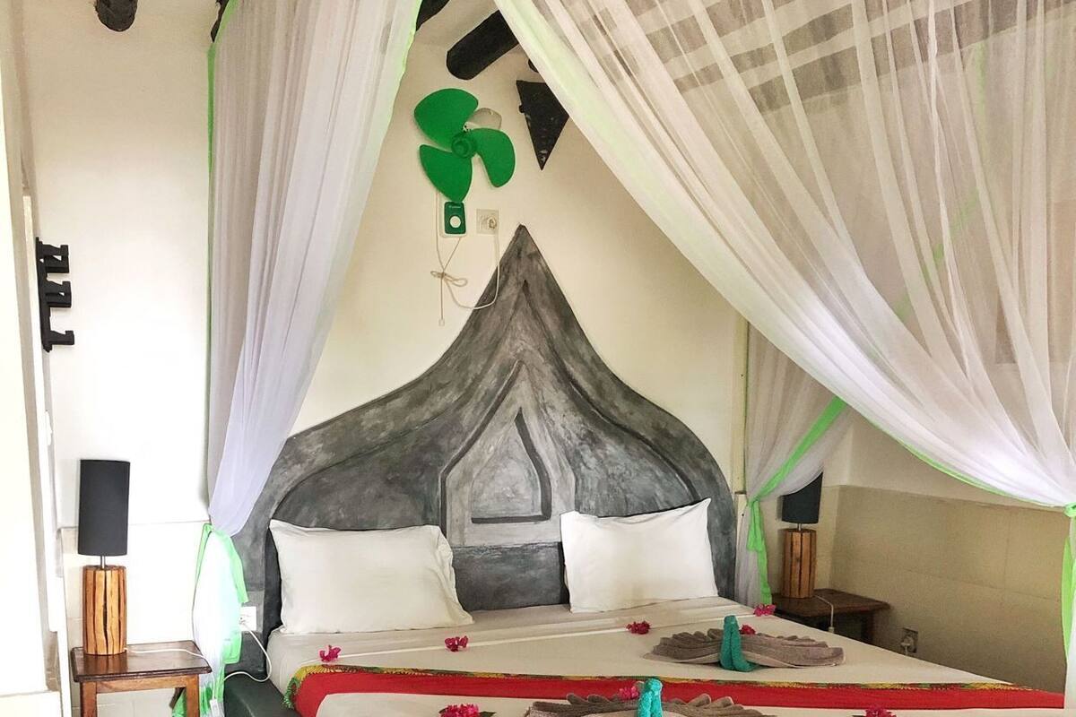A bed with a canopy, a bedside table, a lamp, and a wall-mounted decoration.