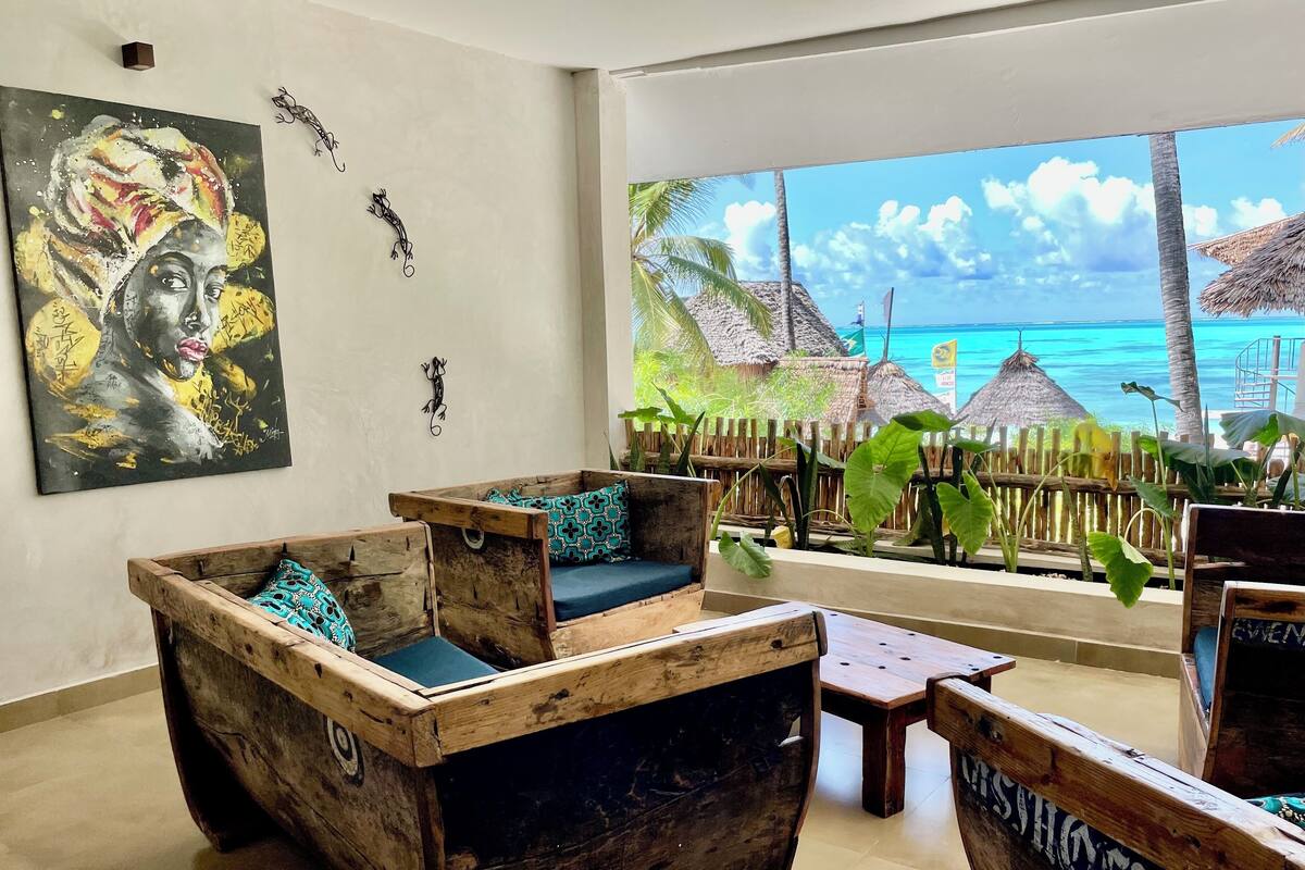 A room with a wooden boat-shaped sofa set and a large window with a view of a beach.
