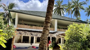 Un edificio de dos pisos con techo de paja, rodeado de palmeras y plantas tropicales.