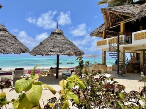 Un complexe hôtelier situé en bord de mer, doté de parasols en chaume, de chaises longues et offrant une vue sur l’océan.