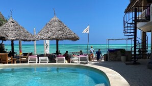 Un área de piscina con una piscina azul cristalina, sillas de descanso y sombrillas de paja.