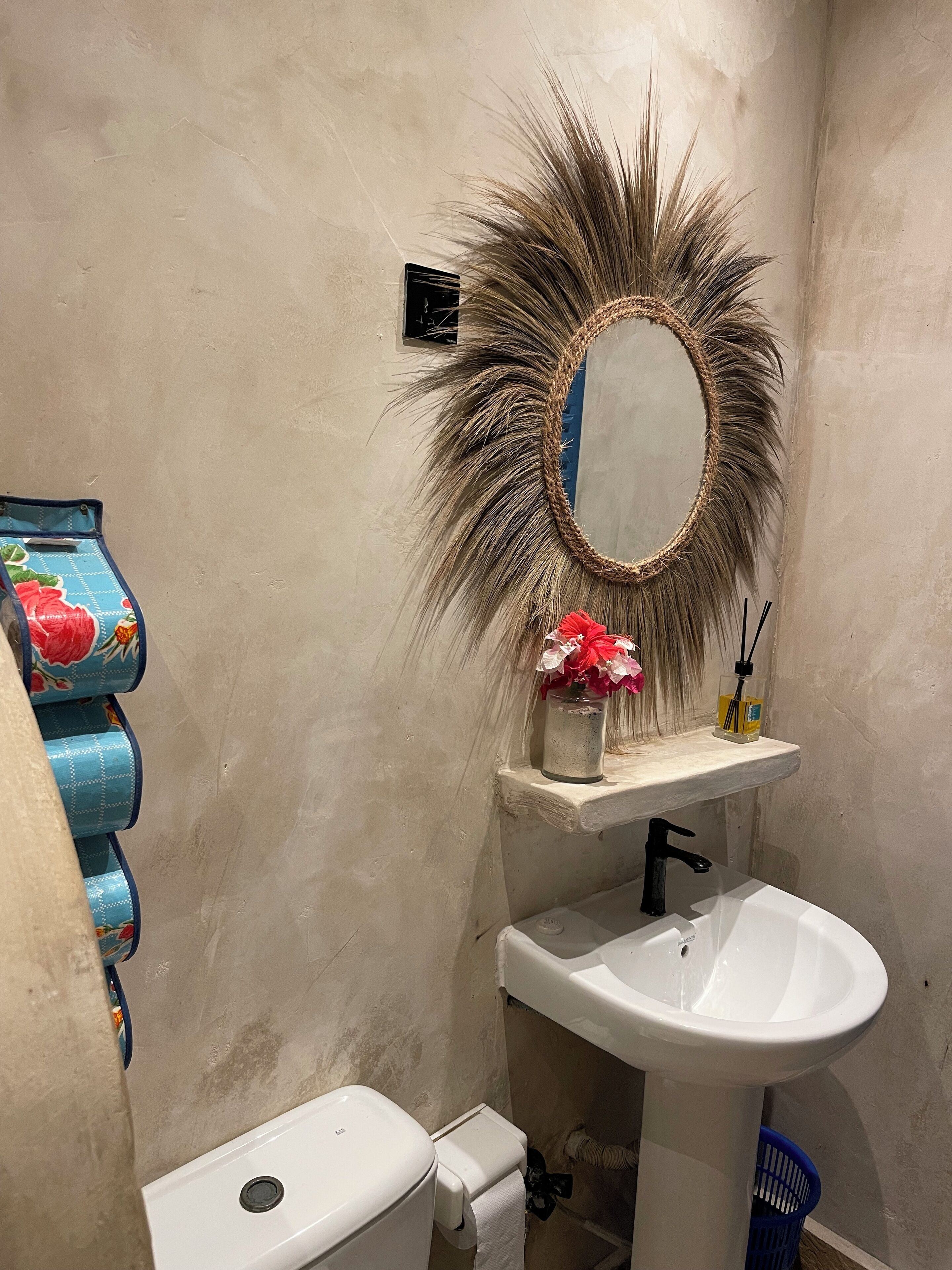 Un baño con un lavamanos blanco, un espejo con marco decorativo, un inodoro y un dispensador de toallas azul.