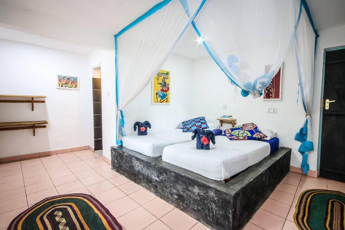 A room with two beds, a bench, a door, and artwork on the walls.
