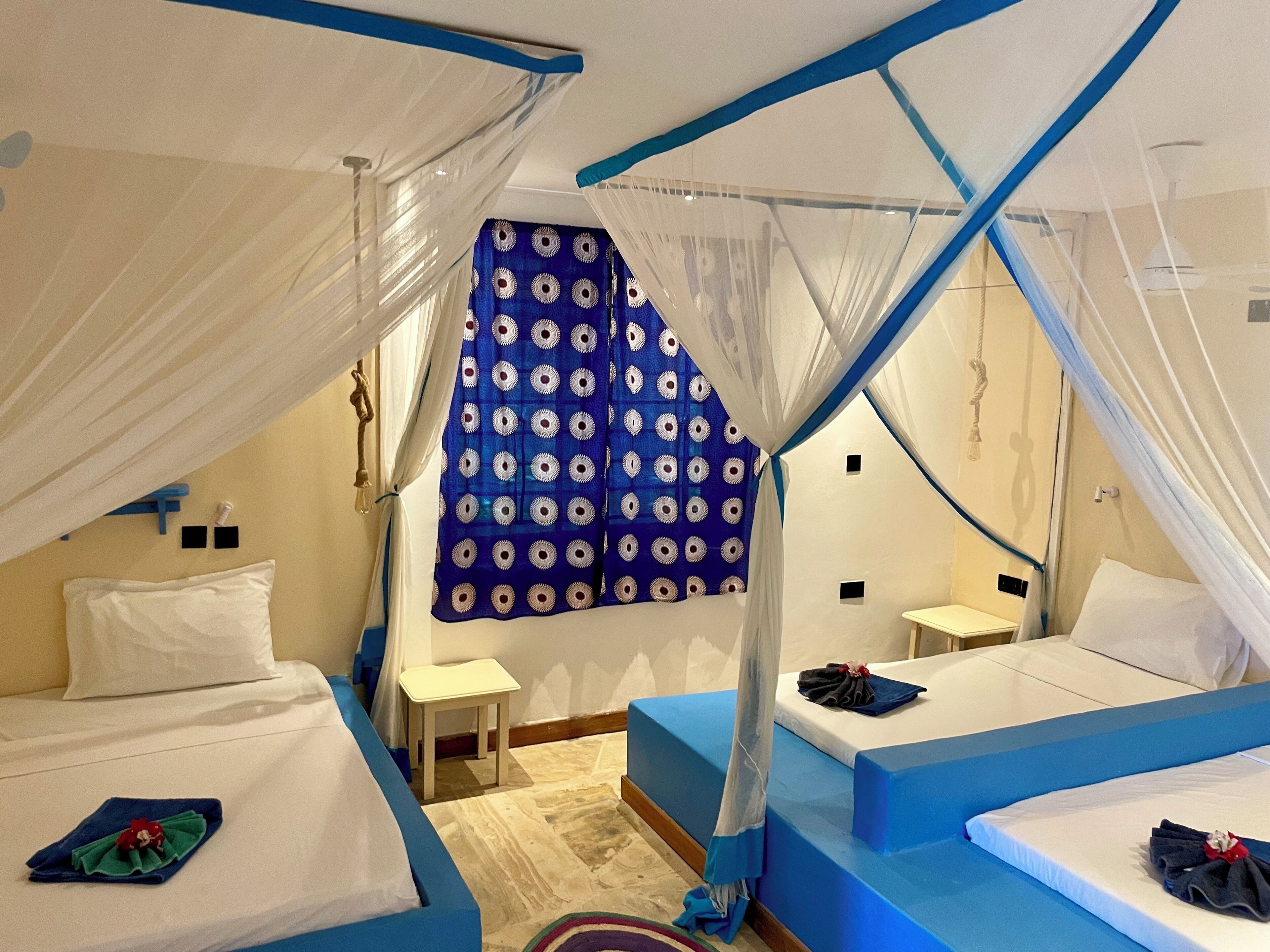 Quarto com duas camas, uma mesinha e cortina com padrão circular.