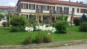 Een gebouw met twee verdiepingen en een balkon, omgeven door een verzorgde tuin met witte bloemen.