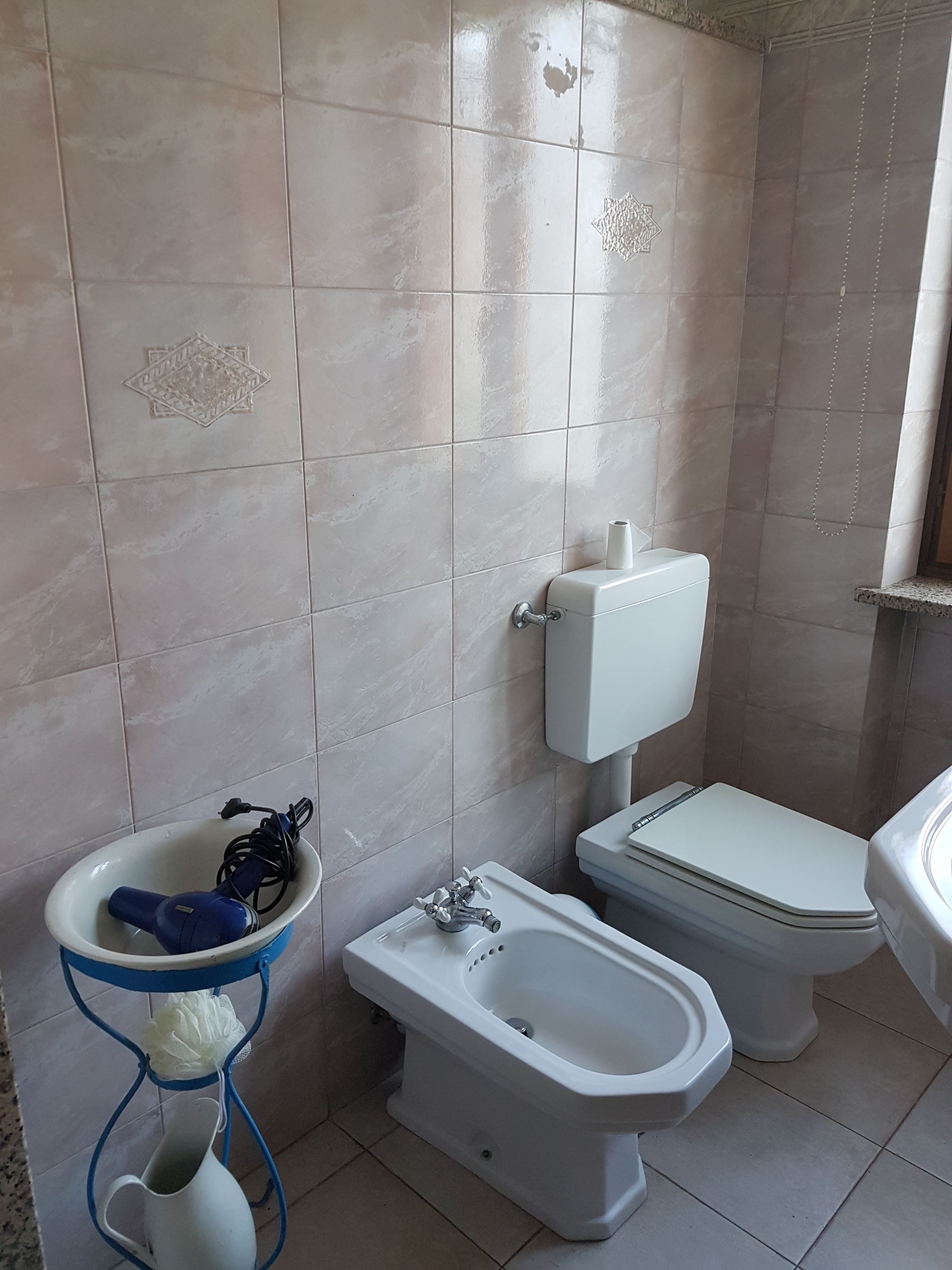 A bathroom with a toilet, bidet, sink, and a blue metal stand with a white pitcher.