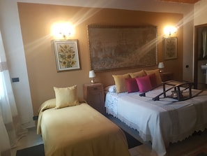A hotel room with two beds, a large painting on the wall, and a small table with a lamp. - B&B La Crota (Asti)