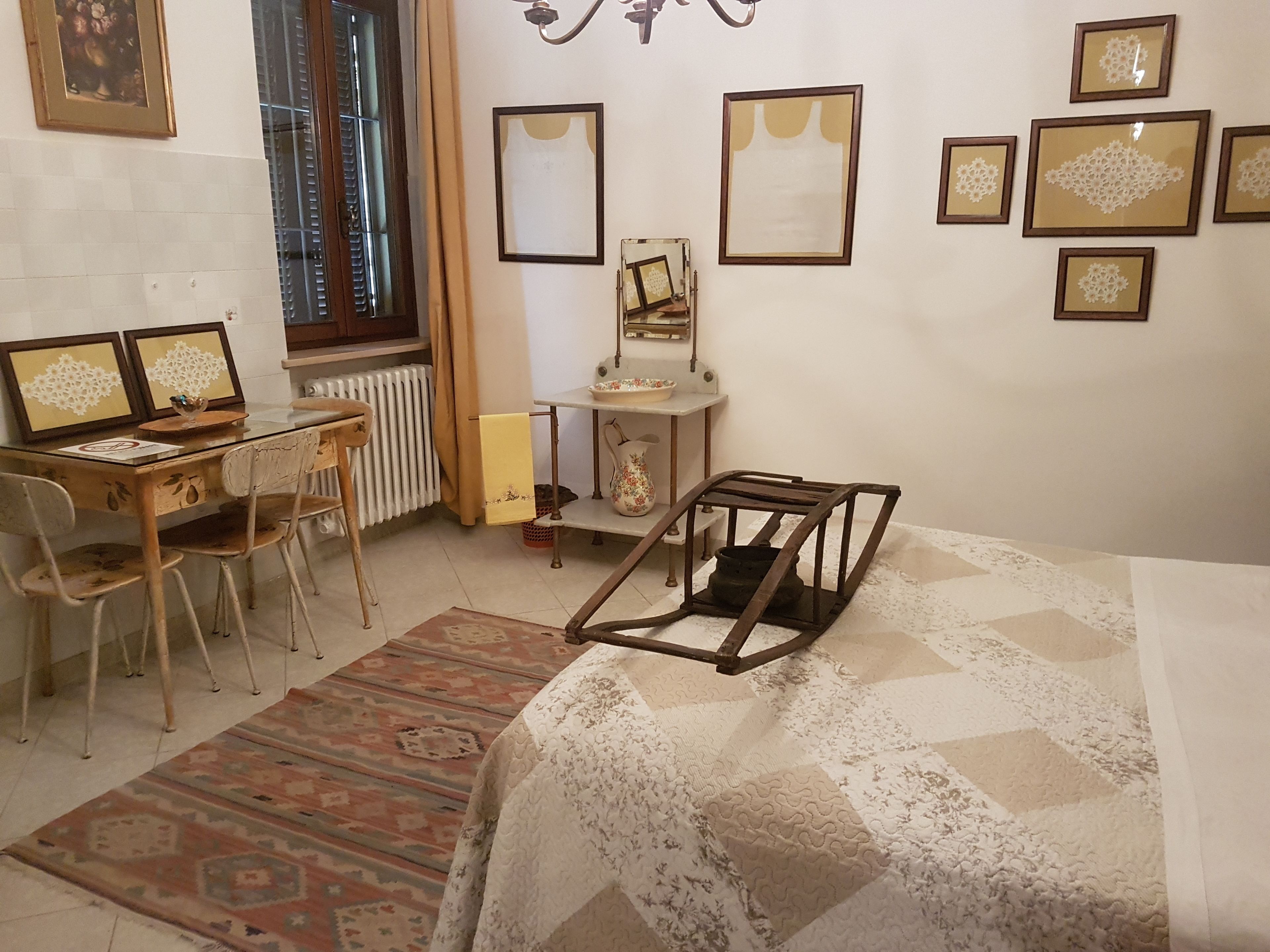 Ein Zimmer mit einem Bett, einem Schreibtisch mit zwei Bildschirmen, einem Stuhl, einem Heizkörper und mehreren gerahmten Bildern an der Wand.