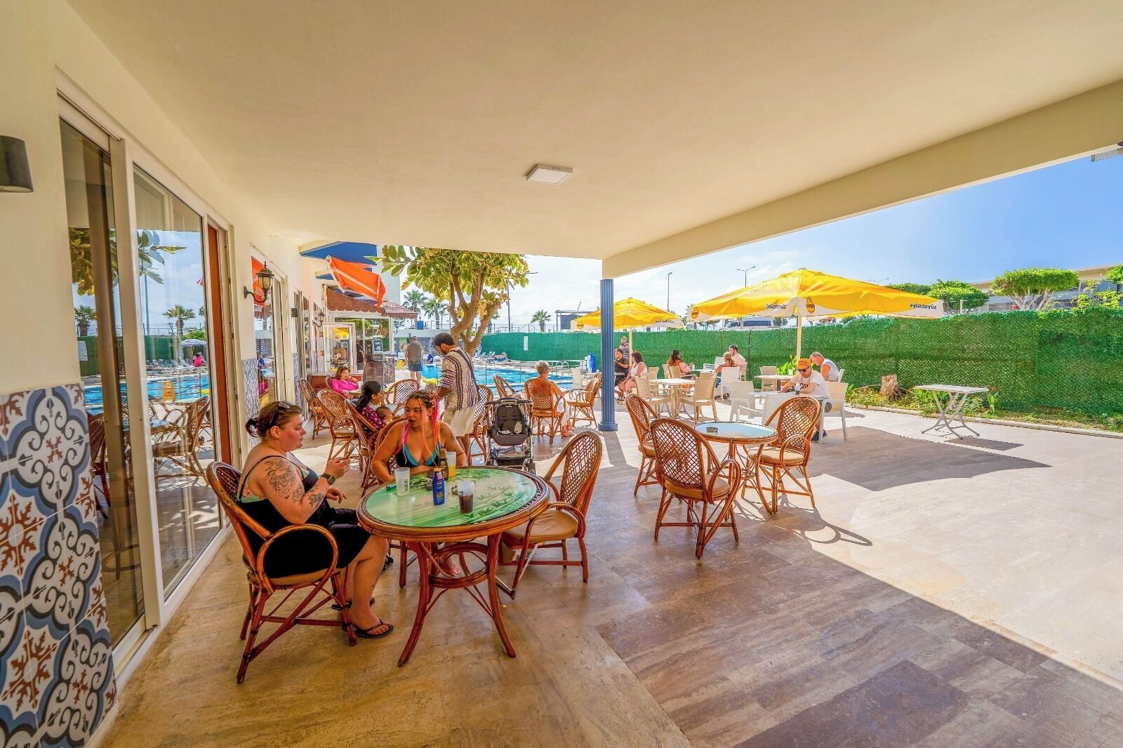 Un patio al aire libre con sillas y mesas de mimbre, una piscina al fondo y vista al mar.