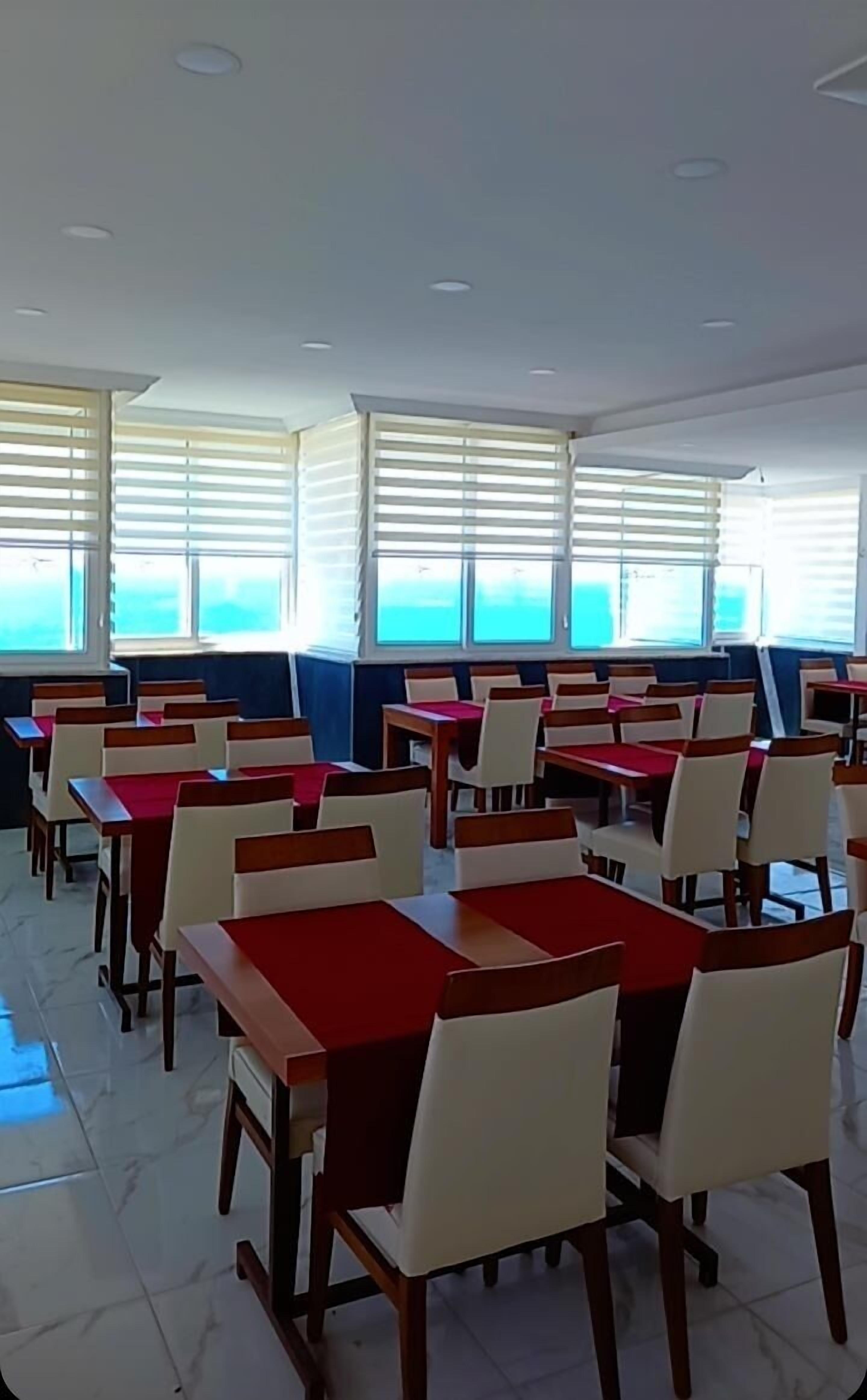 A dining area with tables and chairs, large windows, and a tiled floor.