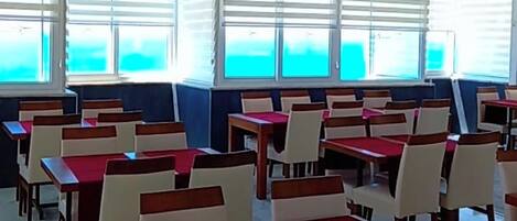 A dining area with tables and chairs, large windows, and a tiled floor.
