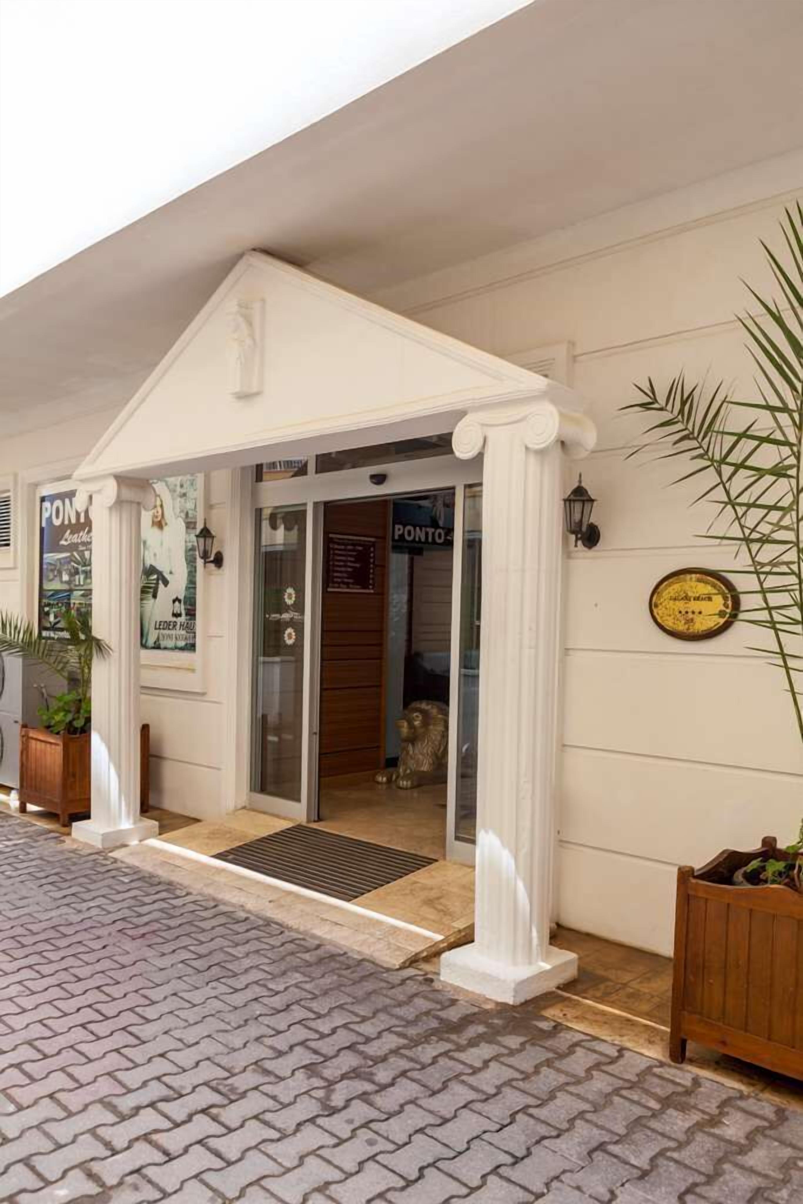 A hotel entrance with a white facade, a glass door, and a small porch area.