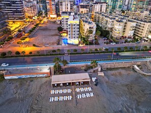 An aerial view of a hotel with multiple floors, a parking area, and a beachside location with sun loungers. - Galaxy Beach Hotel (Alanya)