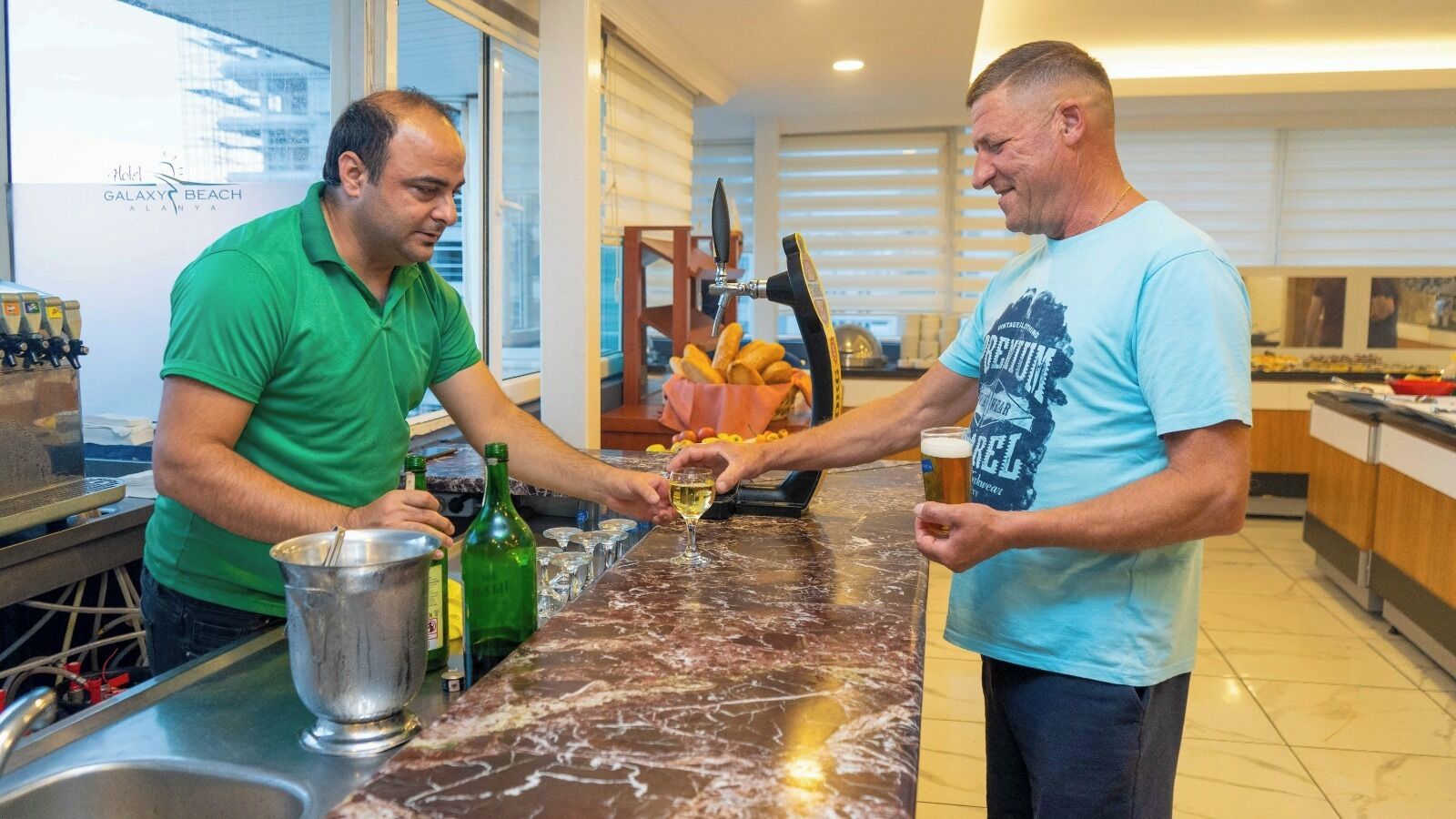 Two men in a kitchen, one pouring a drink into a glass.