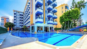 Zona de piscina con un edificio que tiene varios balcones y un área con sillas de playa.