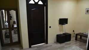A room with a wooden door, a television mounted on the wall, a small table, and a patterned rug on the floor. - Porto Franco Residence (Braila)